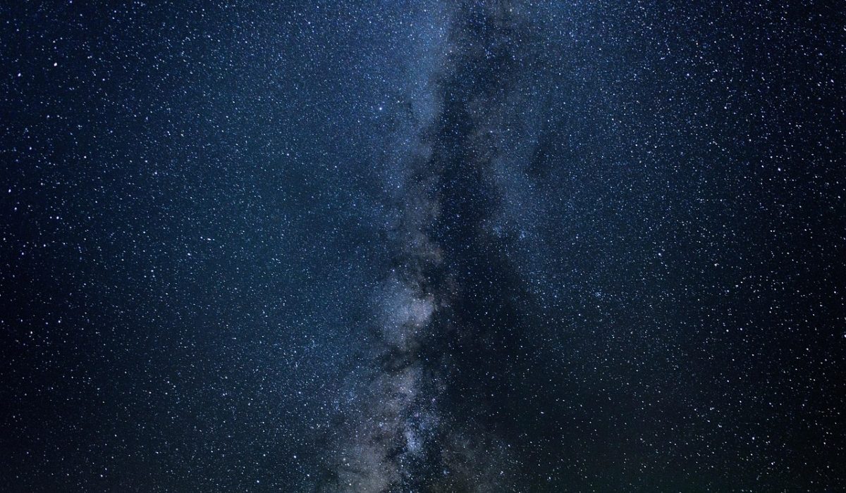 壁纸星座编辑正在多屏电脑前逐张比对壁纸下载素材的实景插画，桌面摊着分类标签与色卡，暖光台灯下氛围安静专注
